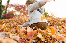 a child playing in fall leaves 