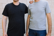 Torso view of two men standing side by side. One is wearing a black pocket tshirt and the other a gray tshirt.