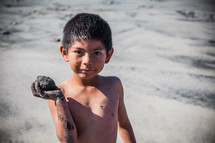 boy child holding a rock on a beach 