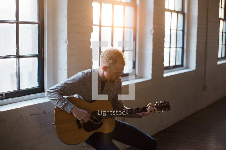 man playing a guitar in front of a window 