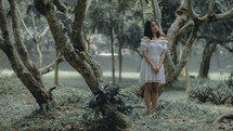 sad woman standing in a forest 