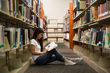woman sitting on a floor of a library reading 