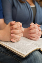 man and woman with their hands held in prayer over an open Bible