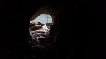 The cross is visible through the opening of a rocky cave in the mountain. 