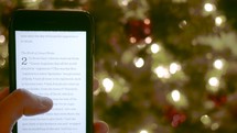 reading scripture from a phone in front of a Christmas tree 