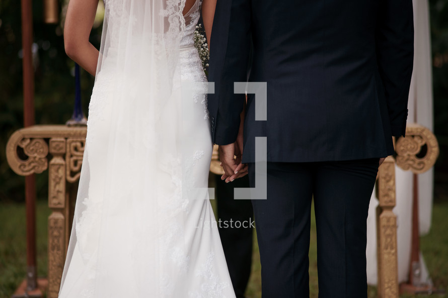 Photograph of a bride and groom exchanging vows, holding hands in front of pastor.