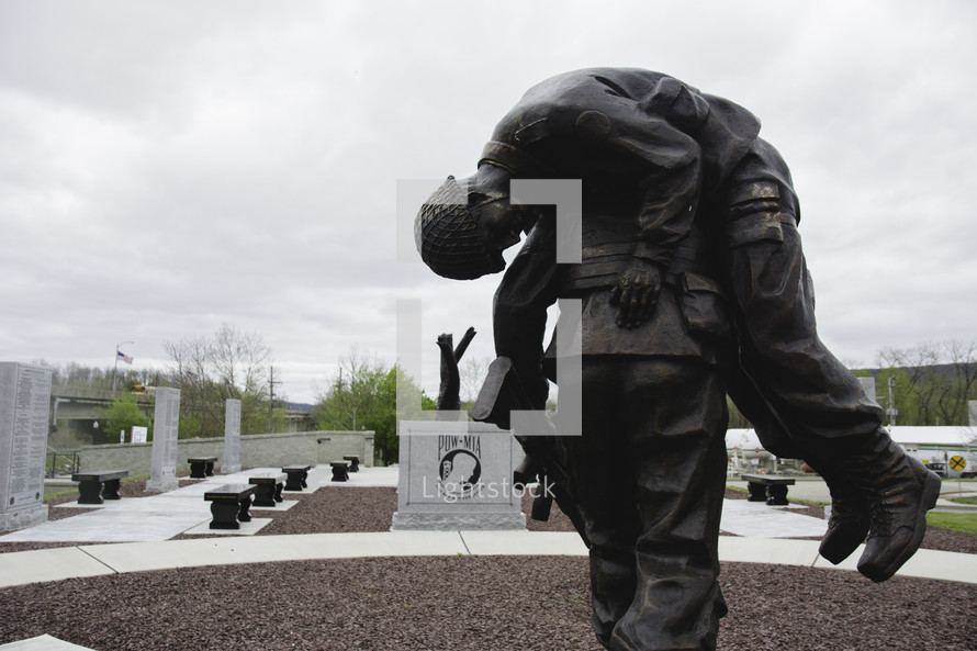 soldier carrying a fallen soldier statue at a memorial 