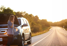 a woman standing next to a car broken down on the side of the road 