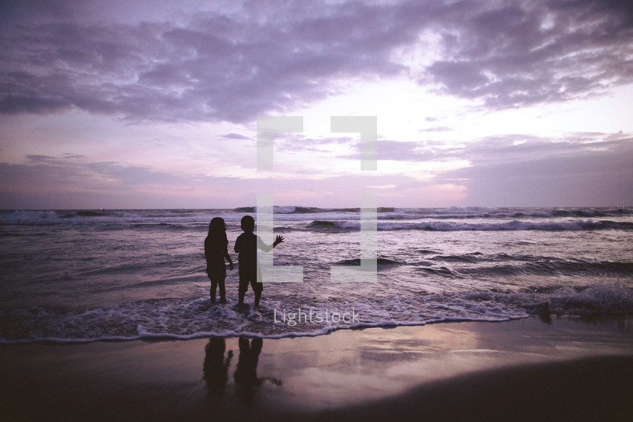 Silhouette of a boy and girl walking along the beach.