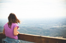 a woman looking over a railing at mountains below 