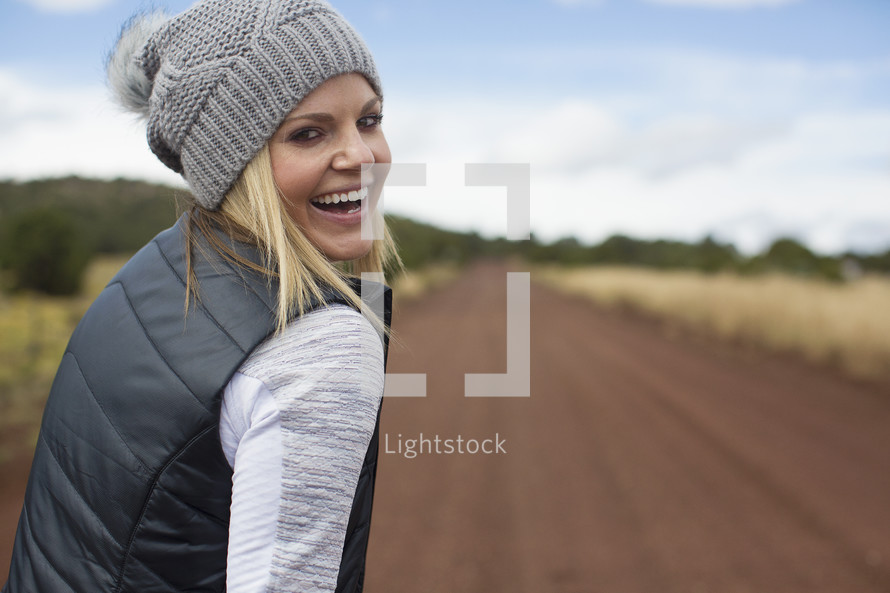 woman looking back while standing in the middle of a dirt road 