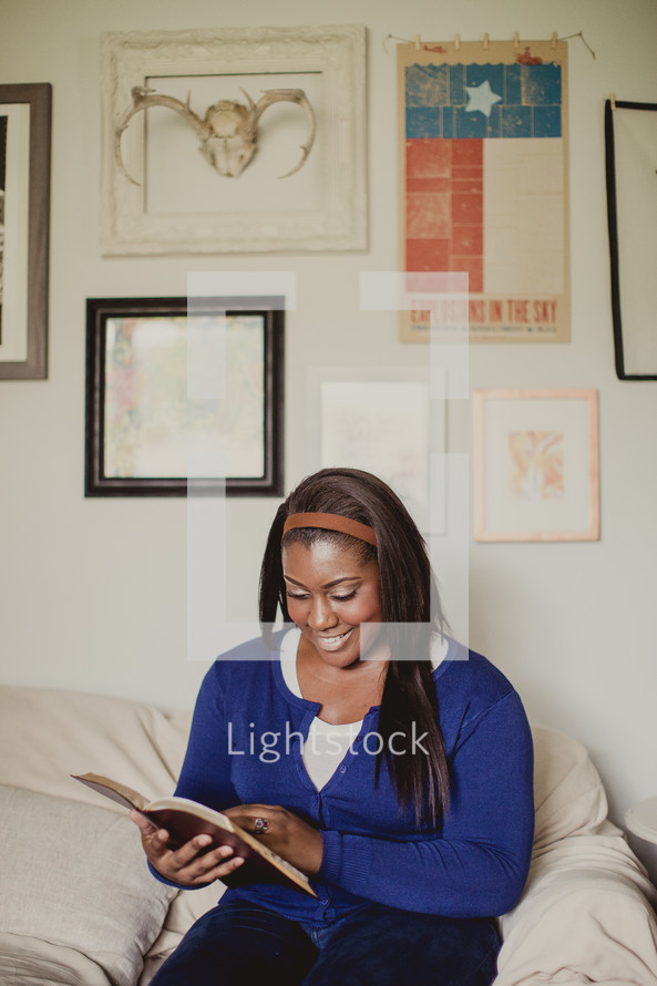 African-American woman reading a Bible on a couch 