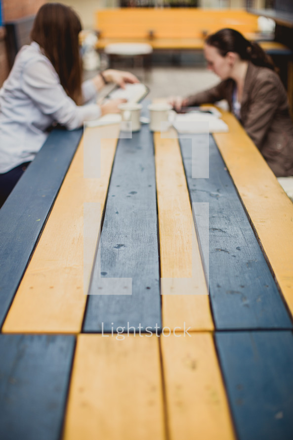 women discussing the Bible while sitting at a picnic table outdoors 