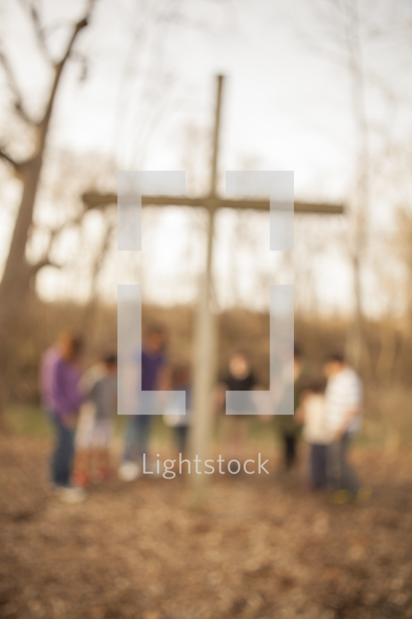 group holding hands and praying around a cross outdoors 