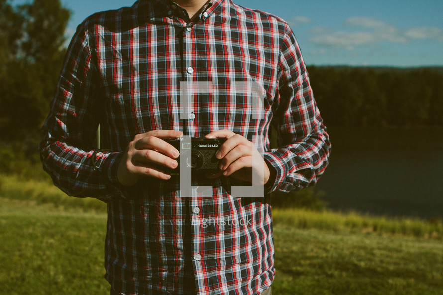 torso of a man in a plaid shirt holding a camera 
