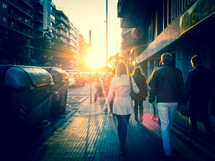 A group of people walking on a city pavement into strong direct sunlight. Cross-processed look.