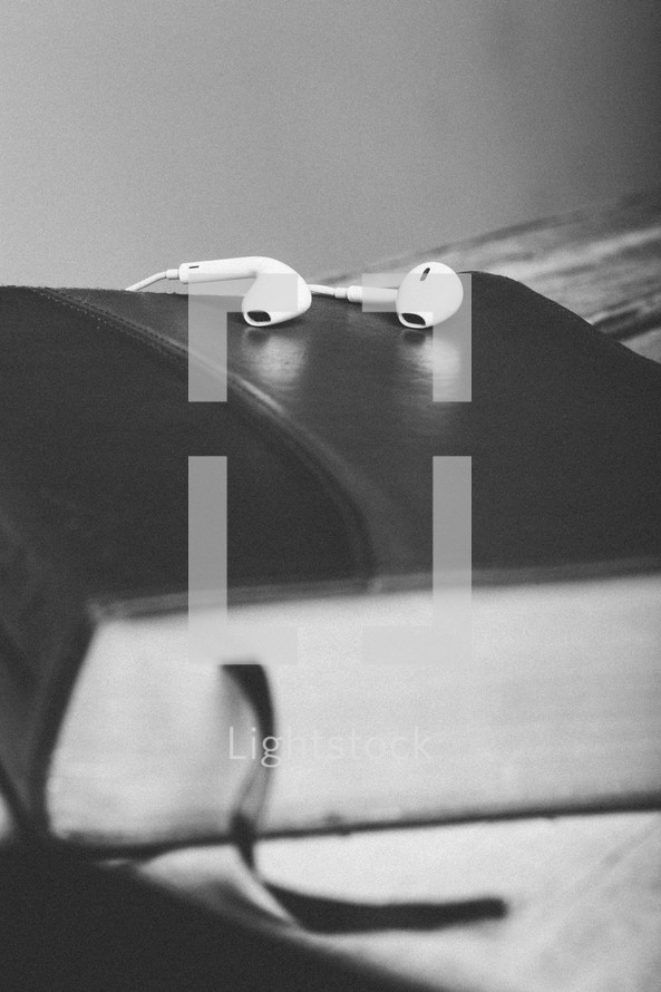Ear buds on top of closed Bible laying on wooden table.