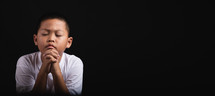 Young Asian boy praying with hands clasped.