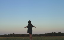 A girl standing alone in a field with her arms outstretched.