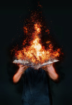 young male holding a burning opened book in sleeveless hoodie 
