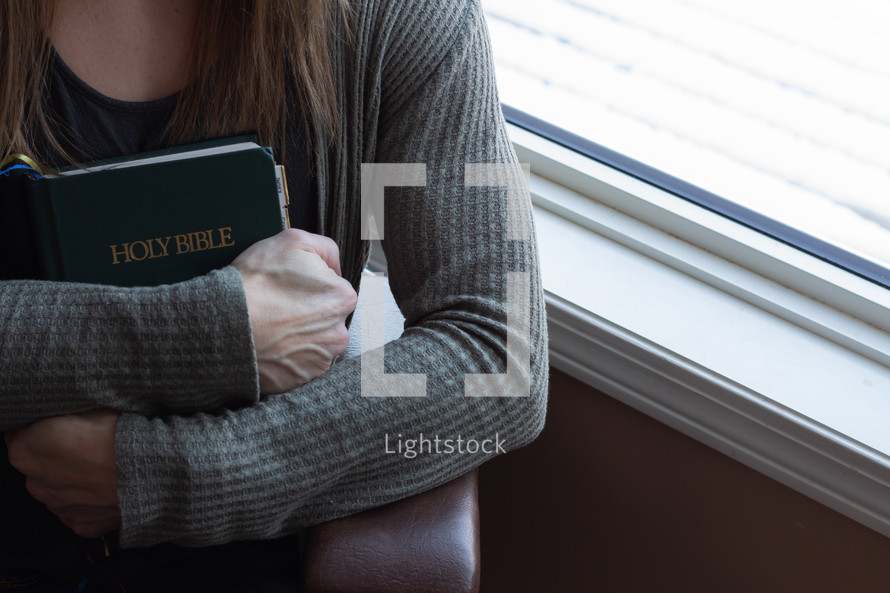A woman holding a Bible close to her heart 