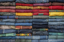 Stack of colorful denim jeans in a variety of shades and patterns, neatly folded and arranged.