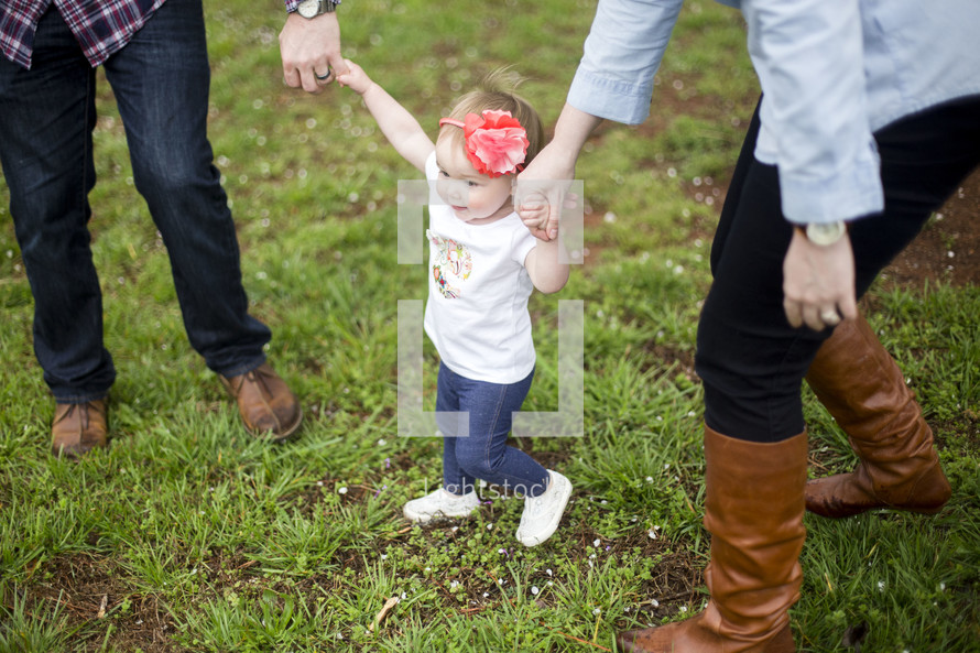 A little girl holds her parent's hands.