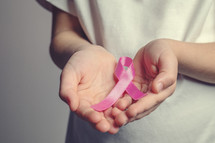 cupped hands holding a pink ribbon 