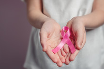 cupped hands holding a pink ribbon 
