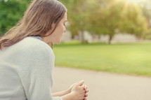 Christian worship and praise. A young woman is sitting and praying on a park bench