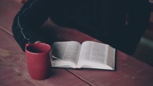 a person sitting reading a Bible with a steaming mug 