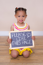 little girl holding up a sign that reads please like this page