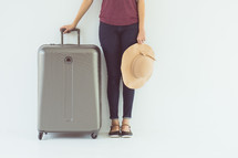 a woman standing with a sunhat and suitcase 