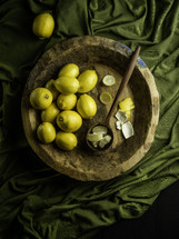 Wooden bowl of lemons on green fabric