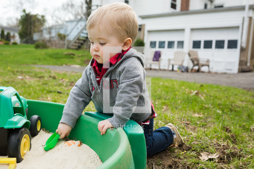 toddler boy playing in a sandbox 