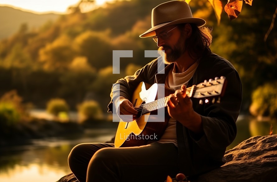 A bearded man, adorned with a hat and glasses, strums a guitar in a natural setting, basking in the soft, warm light of the sunset casting a gentle glow