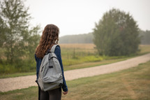 a teen girl standing outdoors with a backpack 