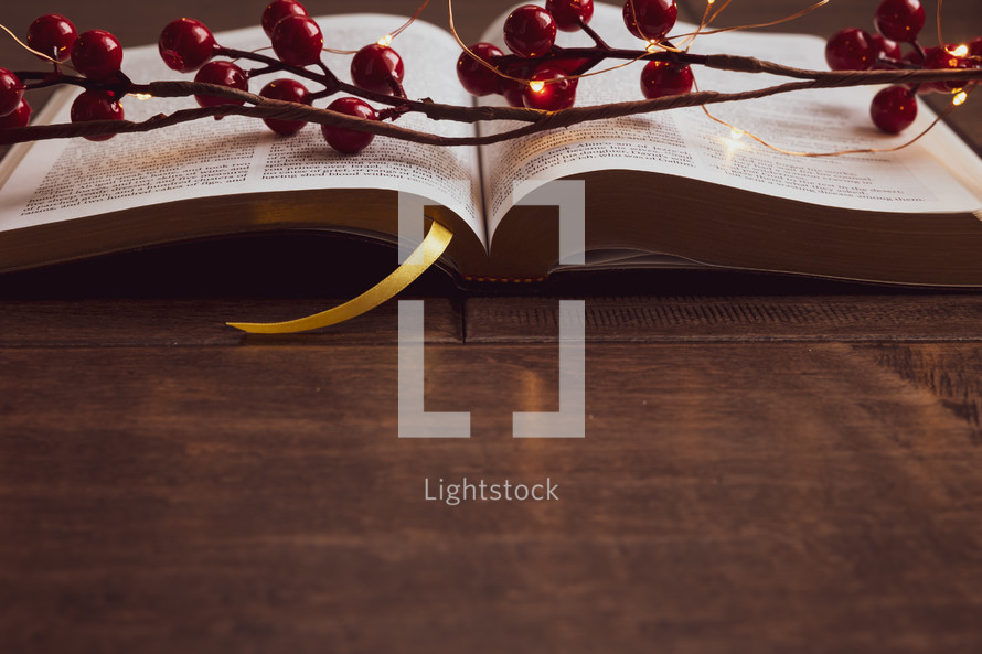open Bible, red berries and fairy lights on a wood background 