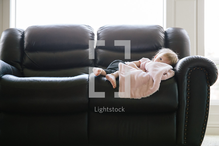 a toddler with a blanket resting on a leather couch 