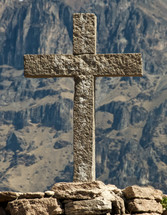A cross of stone against a backdrop of a mountain.