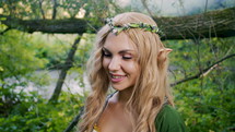 Portrait of young woman in cosplay elf clothes and with make-up on green background. Fantastic look, long blonde hair, forest crown. Halloween concept. High quality 4k footage
