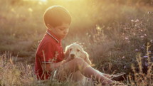 Cute little boy talking with golden retriever puppy on countryside nature background. Golden hour, sunset light. Child stroking dog. Happy lovely pet, new member of family. High quality 4k footage