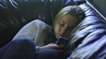 A bored teenager staring at her cell phone while laying on a couch