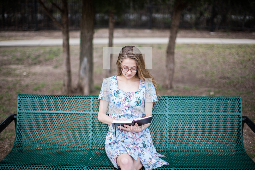 young woman reading a Bible on a bench 