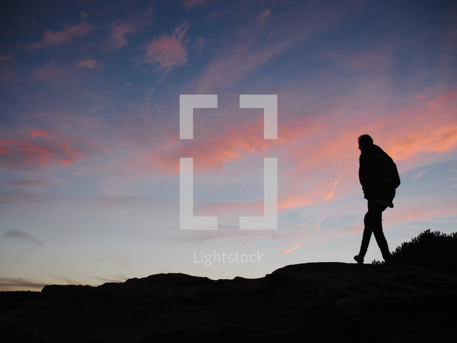 silhouette of a person walking on rocks at sunset 