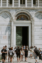 Tourists going in and out of the entrance to an ornate cathedral.