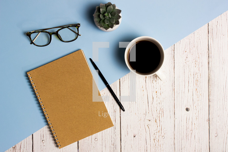 Working items with notebook, pencil, coffee cup and cactus over the blue and wooden background.  