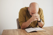 man with her head bowed in prayer over a BIble