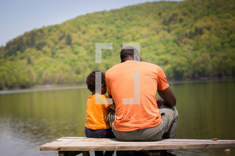 father and son sitting on a bench by a pond 