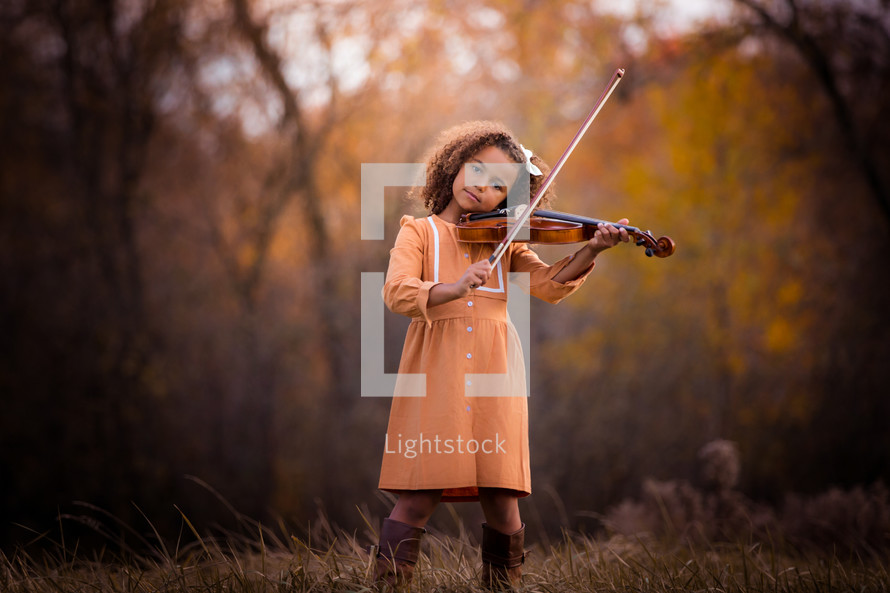 a little girl playing a violin in the woods 